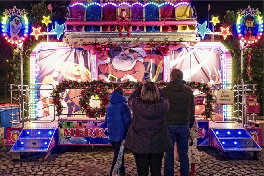 A single child on a Christmas fairground ride being watched by her family