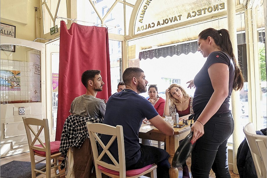 A group of young people at an Italian restaurant discuss menu options with the waitress.